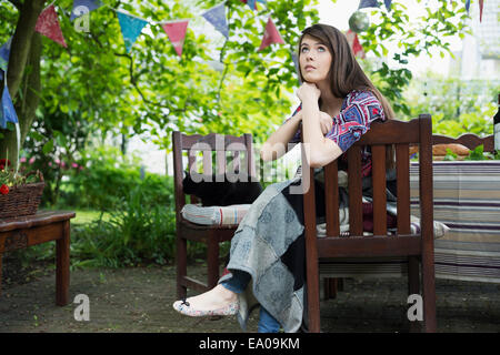 Nachdenkliche junge Frau sitzt im Garten Stockfoto