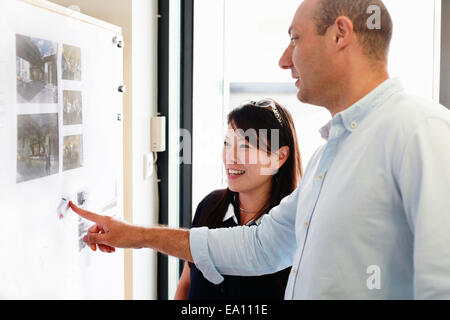 Männliche und weibliche Architekten betrachten Blaupausen auf Büro an der Wand Stockfoto