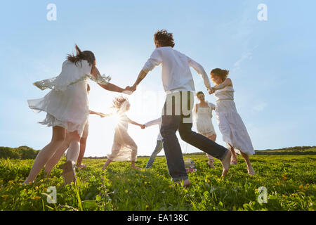 Gruppe von jungen Erwachsenen Freunden spielen Ring-a-Rosie im Feld Stockfoto