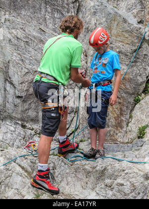 Ein kleiner Junge mit seinem Kletterlehrer immer bereit, eine Felswand zu erklimmen.  Helm, nutzbar zu machen und Kletterschuhe Stockfoto