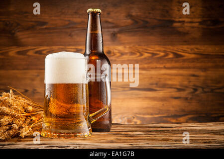 Glas und Flasche Bier mit Ähren auf Holzbohlen Stockfoto