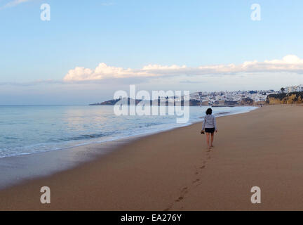 Frau zu Fuß verlassen Fußabdrücke Strand bei Sonnenuntergang, Albufeira. Algarve, Portugal. Stockfoto