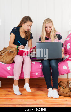 zwei Teengirls sitzt auf Bett machen Hausaufgaben zusammen mit Schulbüchern und laptop Stockfoto