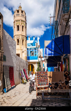 Mann fährt ein Moped auf Straße mit der achteckigen Minarett der Zaouia Zakkak im Hintergrund in der Medina von Sousse, Tunesien Stockfoto
