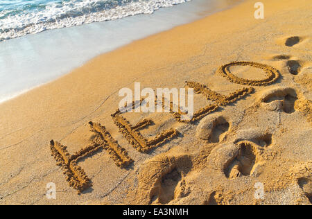 Text Hallo Gruß in Handschrift geschrieben in einem tropischen Sandstrand Stockfoto