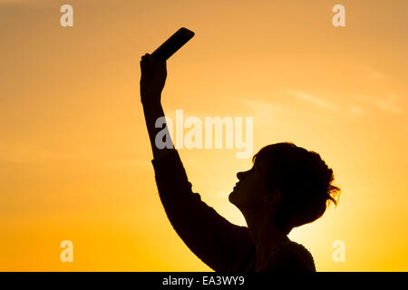 Eine Silhouette Mädchen hält ein Handy in die Luft zu versuchen und ein Datensignal erhalten. Stockfoto