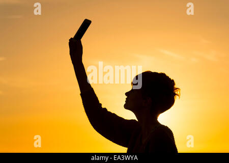 Eine Silhouette Mädchen hält ein Handy in die Luft zu versuchen und ein Datensignal erhalten. Stockfoto