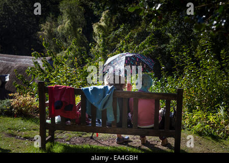 Zwei ältere Damen Schatten selbst Form der Sonne mit einem Regenschirm während sitzen und im Chat außerhalb auf einer Holzbank. Stockfoto