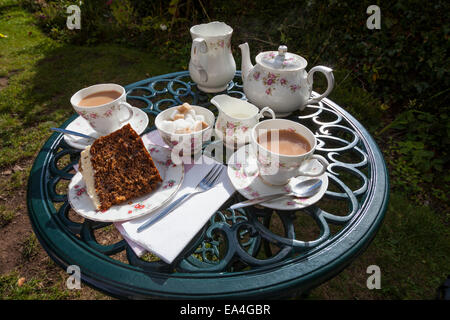 Delicious suchen Stück Karottenkuchen mit zwei Tassen Tee serviert in einem China-Tee-Service auf einem reich verzierten Metall Gartentisch. Stockfoto