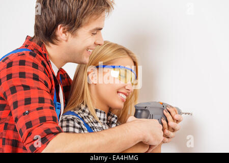 Lächelnd Mechaniker hilft Frau Bohrer verwenden Stockfoto