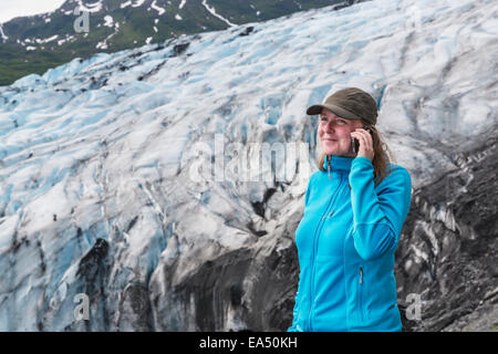 Frau im Gespräch auf einem Handy vor Shoup Gletscher, Shoup Bay State Marine Park, Prinz-William-Sund; Valdez, Alaska, USA Stockfoto