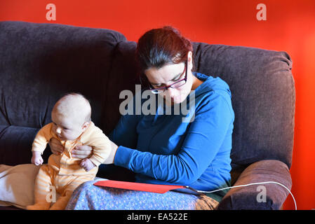 Eine Mutter im Pyjama mit einem Ipad und ignoriert ihr schreiendes baby Stockfoto