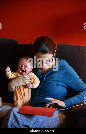 Eine Mutter im Pyjama mit einem Ipad und ignoriert ihr schreiendes baby Stockfoto