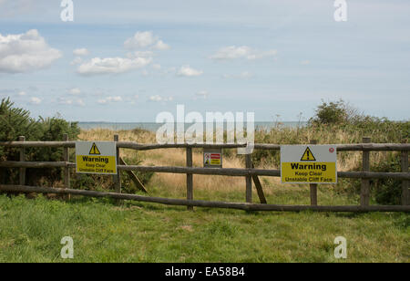 Ein Zaun und Warnzeichen, Fußgänger auf dem Küstenpfad Essex zu halten klar von der instabilen Klippe durch Meer erosion Stockfoto