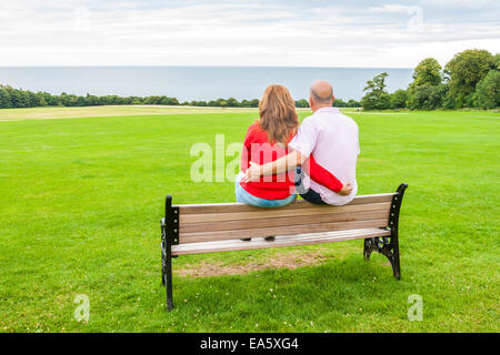 Rückansicht des mittleren Alters paar sitzt auf einer Bank mit Blick auf das Meer Stockfoto