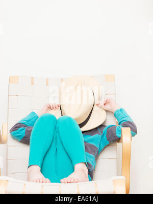 Mädchen 4 bis 5 Jahre im Stuhl sitzen und Gesicht hinter einem Hut versteckt. Stockfoto