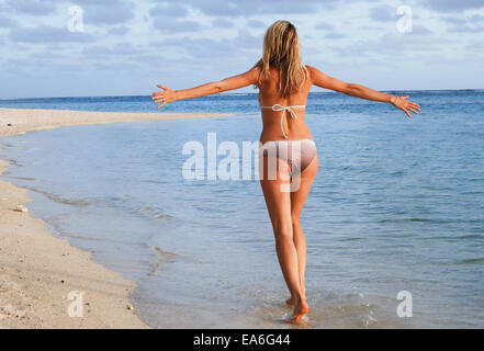 Rückansicht der Frau, die mit ausgestreckten Armen am Strand entlang läuft Stockfoto