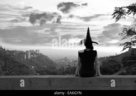 Silhouette einer Frau sitzt auf einer Mauer mit Hexen Hut Stockfoto