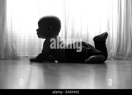 Silhouette eines Jungen, der auf dem Boden bei einem Fenster liegt Stockfoto