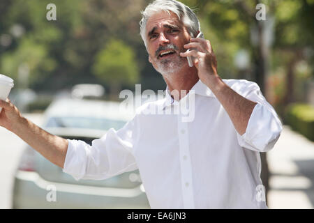 Geschäftsmann versucht, Taxi Hagel während des Gesprächs am Telefon Stockfoto