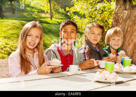 Glückliche Kinder trinken Tee mit cupcakes Stockfoto