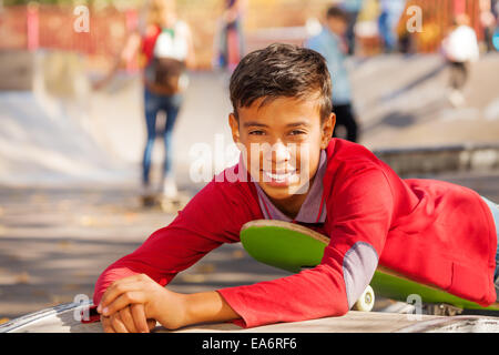Fröhlicher arabischer junge im roten Hemd legt auf skateboard Stockfoto