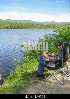 Ein Mann mittleren Alters senior entspannt sich in einen weichen Campingstuhl, raucht eine Zigarre während des Fischens in Pearl Lake in Lissabon, New Hampshire. Stockfoto