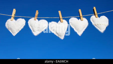 verschiedene weiße Hand genäht Stoff Herzen hängen an der Leine vor blauem Himmel Stockfoto