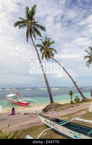 Ein einsamer Urlauber sitzt auf den weißen Sandstrand an der Alona Beach, ein tropisches Paradies auf Panglao Island, Bohol, Philippinen. Stockfoto