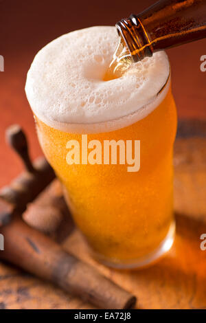 Ein Glas kaltes Bier auf einem rustikalen Fass mit antiken Zapfen gegossen wird. Stockfoto