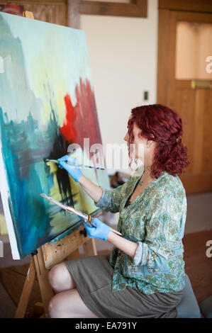Frau mittleren Alters halten Palette und malen auf Leinwand Stockfoto