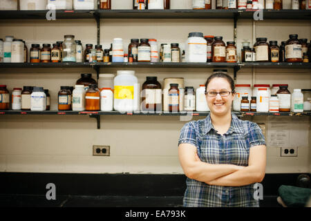 Porträt der lächelnde Frau mittleren Erwachsenenalter an Wand montiert Regale mit Laborflaschen Stockfoto