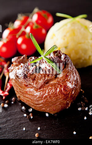 Stück rotes Fleisch Steak mit Rosmarin auf schwarzen Steinoberfläche serviert. Stockfoto