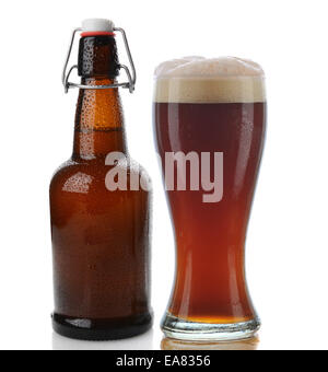 Nahaufnahme von einem Glas dunkles Bier mit einem schaumigen Kopf neben einer Schaukel Top braune Bierflasche. Geradeaus weiter Schuss auf weißem Hintergrund Stockfoto