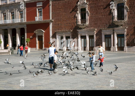 Jugendliche tummeln sich mit einer Herde von Tauben auf der Plaza De La Patria in Aguascalientes, Mexiko Stockfoto