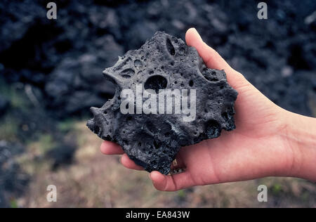 Eine Frau hält ein Stück schwarzen Lavagestein aus einer Eruption in den 1980er Jahren des Vulkans Kilauea auf Big Island von Hawaii, USA. Stockfoto