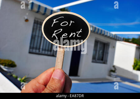 ein Mann Hand hält ein Schild mit dem Text geschrieben vor einem Haus zu vermieten Stockfoto