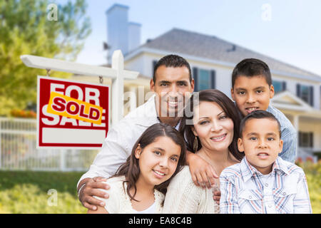 Hispanische Familienglück vor ihrem neuen Haus und verkauft Haus für Immobilien Verkaufsschild. Stockfoto