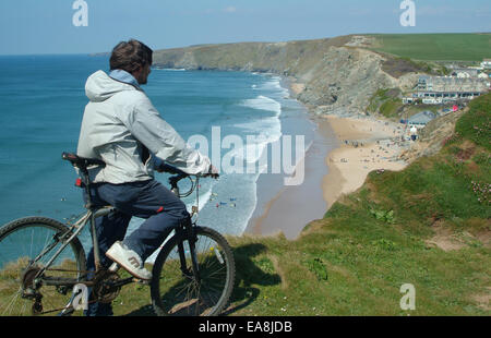 Radfahrer auf Klippe, auf der Suche nach unten am Strand mit freundliches auf Sand & im Meer Surfen Watergate Bay in der Nähe von Newquay Restormel im Norden Stockfoto