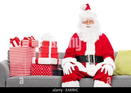 Santa sitzen auf einem Sofa voller Weihnachtsgeschenke auf weißen Hintergrund isoliert Stockfoto