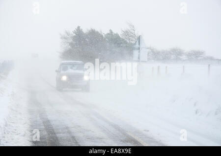 Einen Mietwagen in Blizzard Bedingungen fahren Mönche Weg mit Scheinwerfer auf. Wind weht Schnee über Straße. Stockfoto