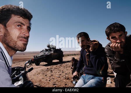 Kurden sind von einem türkischen Armee Fahrzeug inspiziert, wie sie die alliierten Luftangriffe auf die syrische Stadt Kobani, von einem Hügel zu sehen, die mit Blick auf die Stadt, in der Nähe der türkischen Stadt Suruc an der türkisch-syrischen Grenze. Tausende von Kurden wurden gezwungen, die syrische Stadt Kobani aufzugeben, die von islamischen Staat Truppen belagert wird. Die meisten von ihnen Leben in Flüchtlingslagern in der türkischen Stadt Suruc. Stockfoto