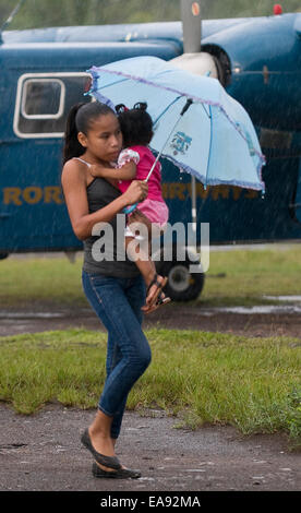 9. November 2014 - Port Jonestown, Guyana. Ein Bewohner von Port Jonestown in der Provinz von Guayana Barima-Waini versucht, ein Kind trocken zu halten, wie sie den lokalen Flughafen als einen Weg in die Stadt nutzt. Es ist eines der Grenzstädte Teil der Nordwesten des Landes, das den Zustrom des Bergbaus für Gold und Bauxit in den dichten Dschungel mit Auswirkungen auf die Umwelt und Infrastruktur der Gemeinde gesehen hat. Bildnachweis: Ralph Lauer/ZUMA Draht/Alamy Live-Nachrichten Stockfoto