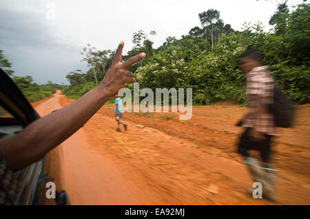 9. November 2014 - Port Jonestown, Guyana. Taxi Fahrer Devon Sealey Wellen zu Einheimischen zu Fuß entlang der Mautstraße zwischen Port Jonestown und Bergbau Stadt von Murphys Ridge in die Barima-Waini Provinz von Guyana. Das Gebiet hat einen Zufluss des Bergbaus für Gold und Bauxit in den dichten Dschungel mit der Mautstraße, die einzige Verbindung gesehen. Die Straße verläuft der Völker-Tempel. Jonestown Gemeinschaft wo 909 Anhänger des reverend Jim Jones ihr Leben nahm. Bildnachweis: Ralph Lauer/ZUMA Draht/Alamy Live-Nachrichten Stockfoto