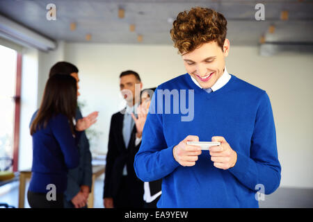 Lächelnde Geschäftsmann mit Smartphone vor einem Kollegen Stockfoto
