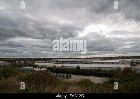 Weite Sicht auf Industrielager vor ländlicher Landschaft, mit weit entfernten Häusern und bewölktem Himmel über einer gemischten Fläche. Stockfoto