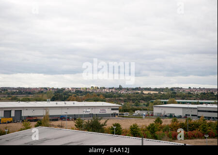 Weite Sicht auf Industrielager vor ländlicher Landschaft, mit weit entfernten Häusern und bewölktem Himmel über einer gemischten Fläche. Stockfoto