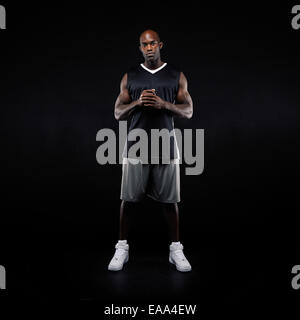 Voller Länge Bild des jungen Basketball-Spieler stehen auf schwarzem Hintergrund. Muskulösen afrikanischen Sportler im Sport einheitlich. Stockfoto