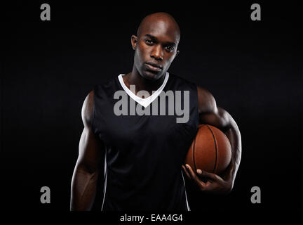 Porträt von zuversichtlich junger Mann mit starken Build mit einem Korb Ball auf schwarzem Hintergrund. Afrikanische männlichen Athleten. Stockfoto
