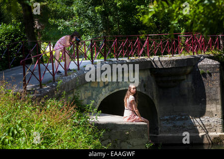 Ein junges Mädchen Fotos ein anderes Mädchen sitzt auf einer alten Flussbrücke bei Jarnac Stockfoto